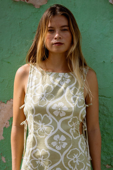 Woman wearing a green floral dress standing against a green wall.