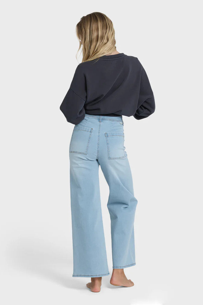 Back view of a woman wearing a charcoal sweater and light blue jeans on a white background