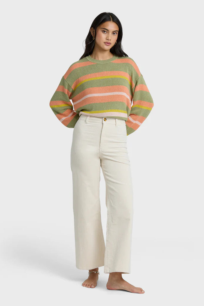Woman wearing a colorful striped sweater and white pants on a white background