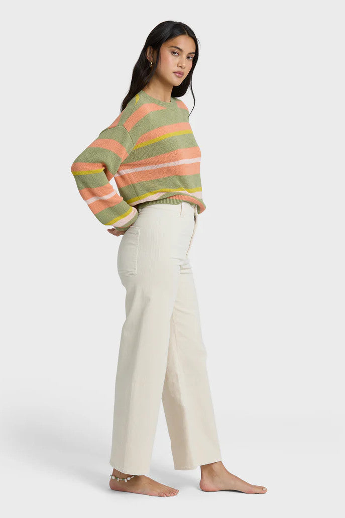 Woman wearing a colorful striped sweater and beige pants on a white background
