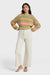 Woman wearing a colorful striped sweater and white pants on a white background