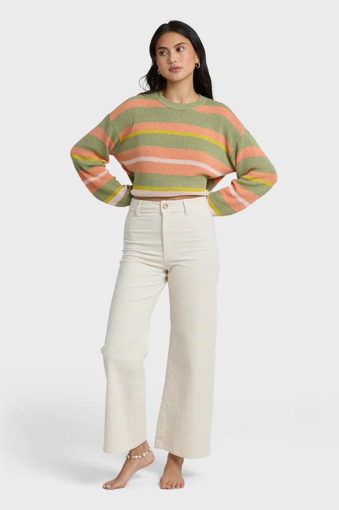 Woman wearing a colorful striped sweater and white pants on a white background