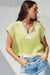 Woman wearing a green and beige striped sweater with blue jeans against a light background