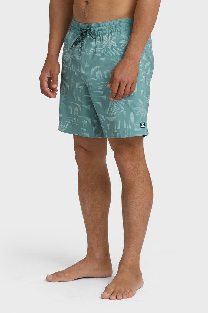 A man wearing teal boardshorts with a palm tree pattern, elastic waist and drawstring on a white background.