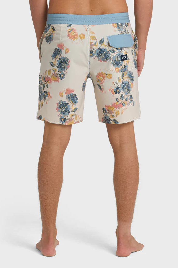 Back view of a man wearing a pair of boardshorts that are primarily cream with a blue, coral, and yellow floral pattern and blue waistband on a white background.