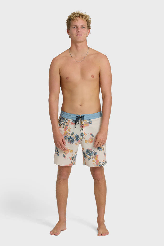 Man wearing a pair of boardshorts that are primarily cream with a lblue, coral, and yellow floral pattern and blue waistband on a white background.