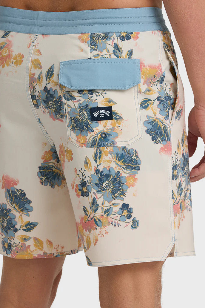 Man wearing a pair of boardshorts that are primarily cream with a lblue, coral, and yellow floral pattern and blue waistband on a white background.