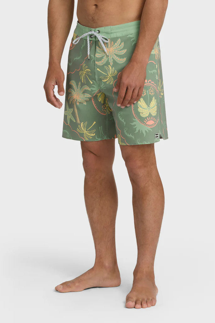 Man wearing a pair of boardshorts that are primarily green with a green, coral, and yellow palm tree and starfish design on a white background.