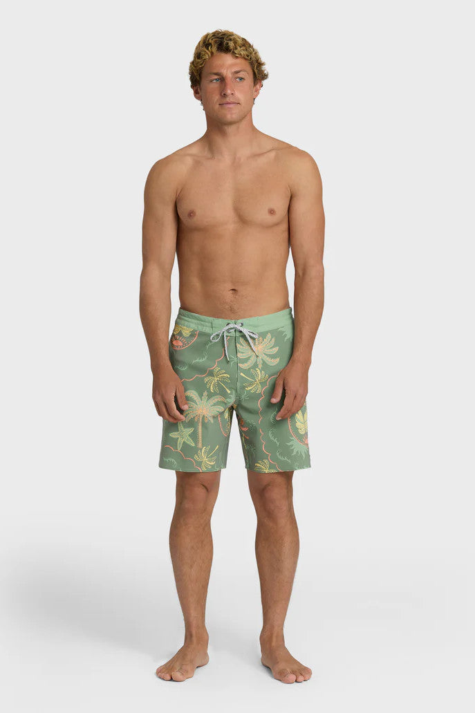 Man wearing a pair of boardshorts that are primarily green with a green, coral, and yellow palm tree and starfish design on a white background.