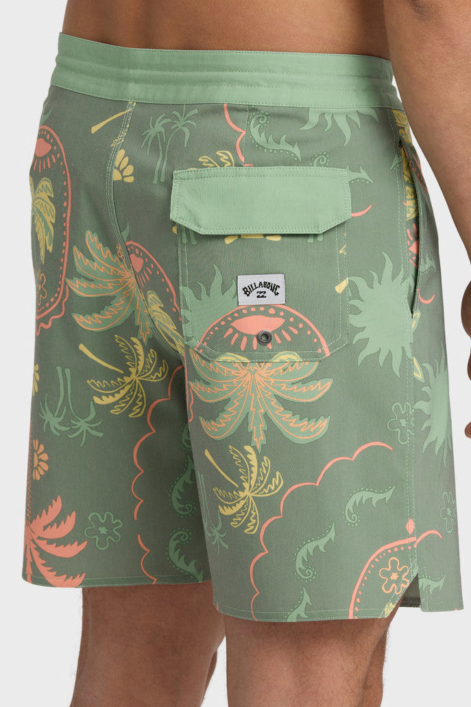 Man wearing a pair of boardshorts that are primarily green with a green, coral, and yellow palm tree and starfish design on a white background.