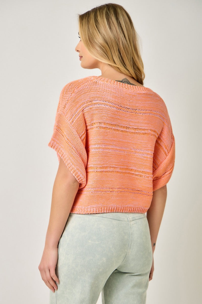 Back view of a woman wearing a coral sweater and light blue pants on a white background