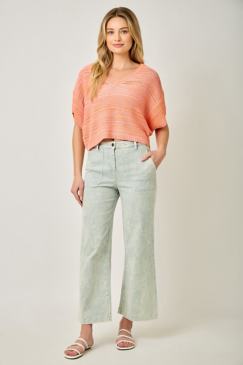 Woman wearing a coral sweater and light blue pants on a white background