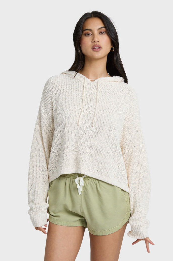 Woman wearing a white knit hoodie and green shorts on a white background