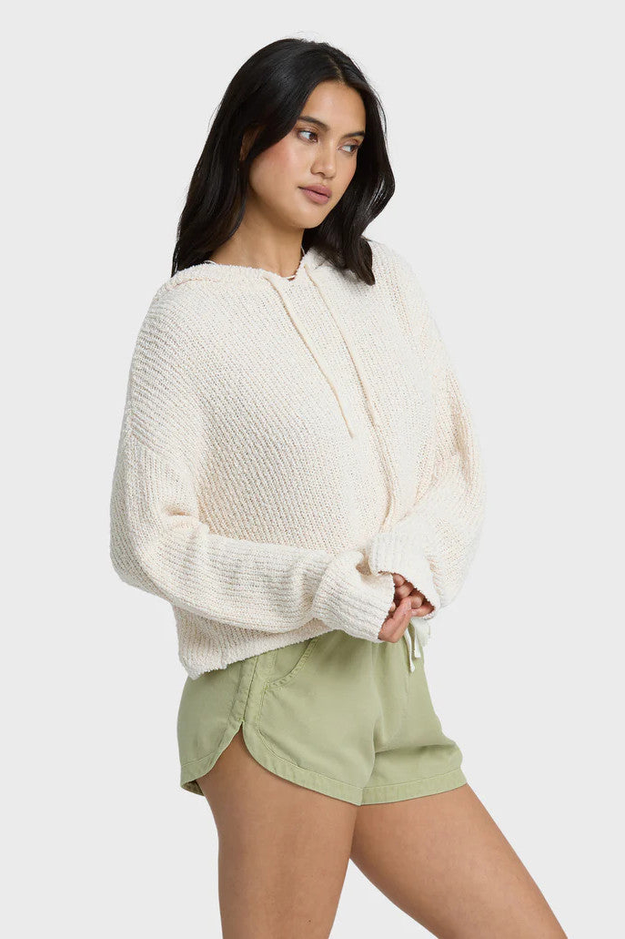 Woman wearing a white knit cardigan and light green shorts on a white background