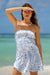 Woman in a strapless blue and white patterned dress standing on a beach.