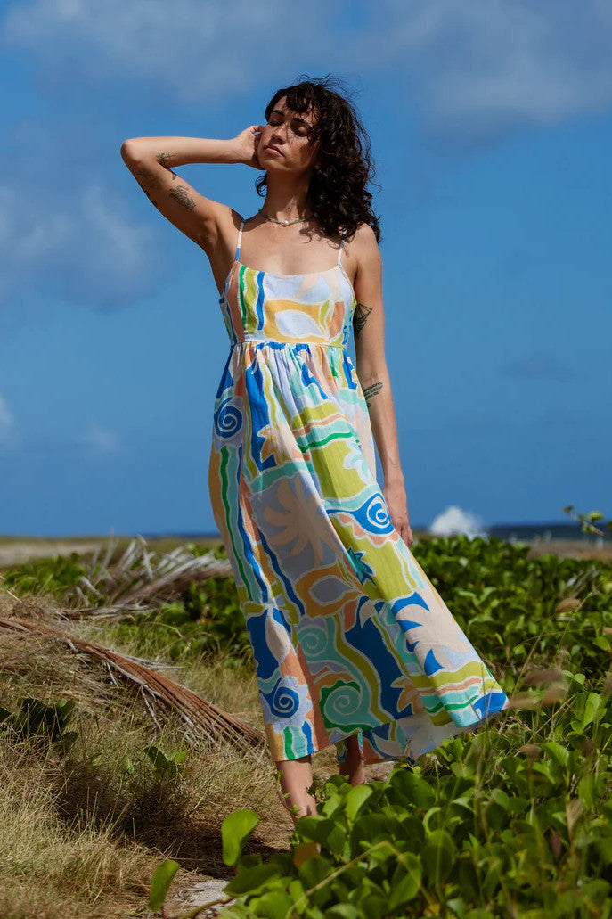 Woman in a colorful dress standing outdoors with a blue sky and greenery in the background