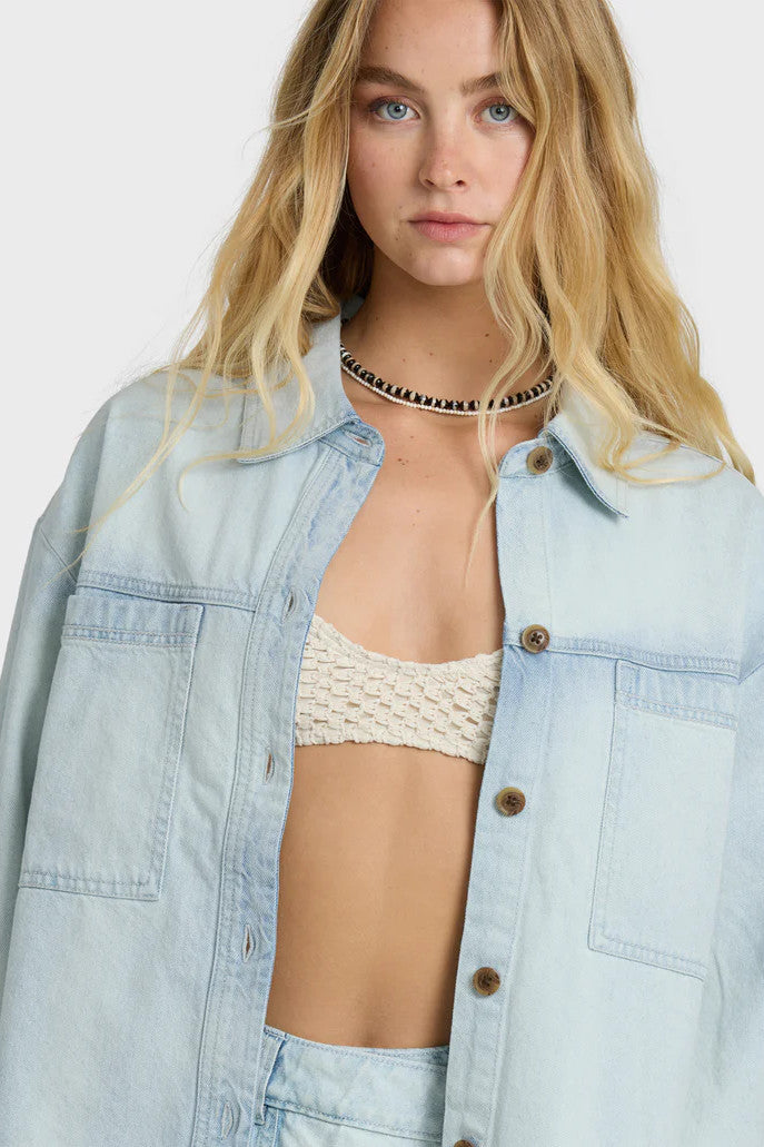 Woman wearing a light blue denim shirt over a bikini on a white background