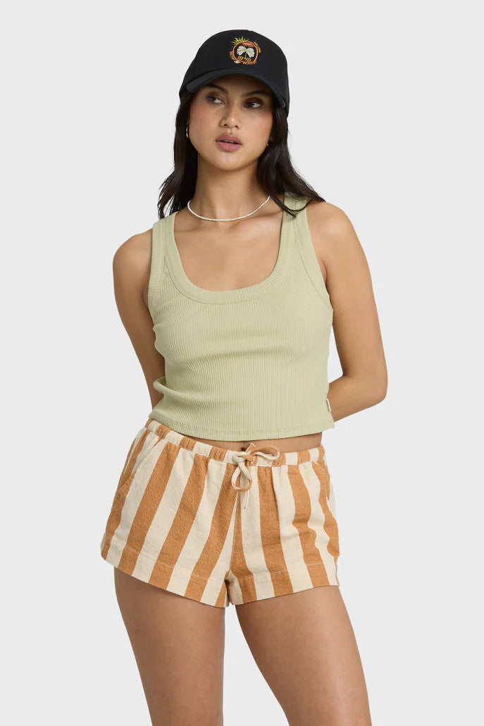 Woman wearing a light green tank top and striped shorts with a black cap on a white background