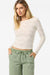 Woman wearing a white long-sleeve top and green pants on a white background