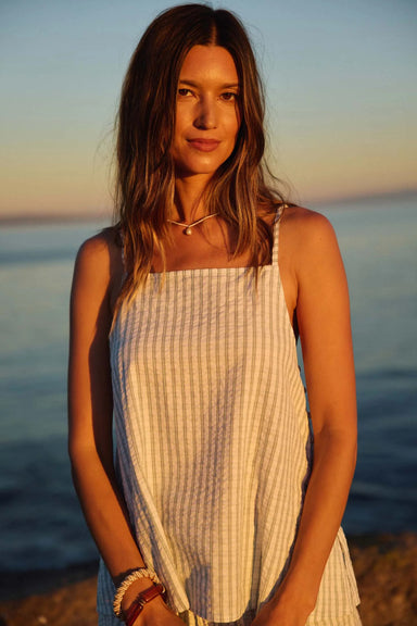 Woman in a white striped tank standing on a beach at sunset