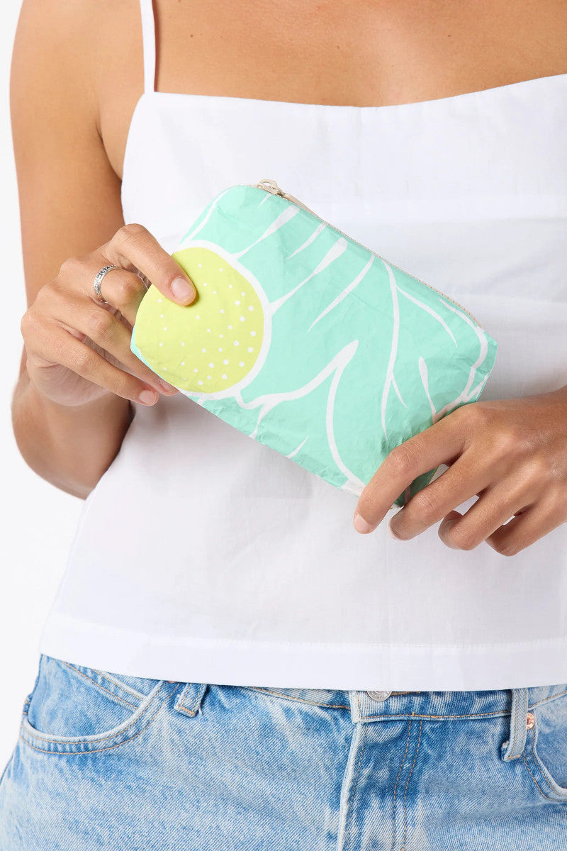 Person holding a green clutch with leaf pattern against a white background