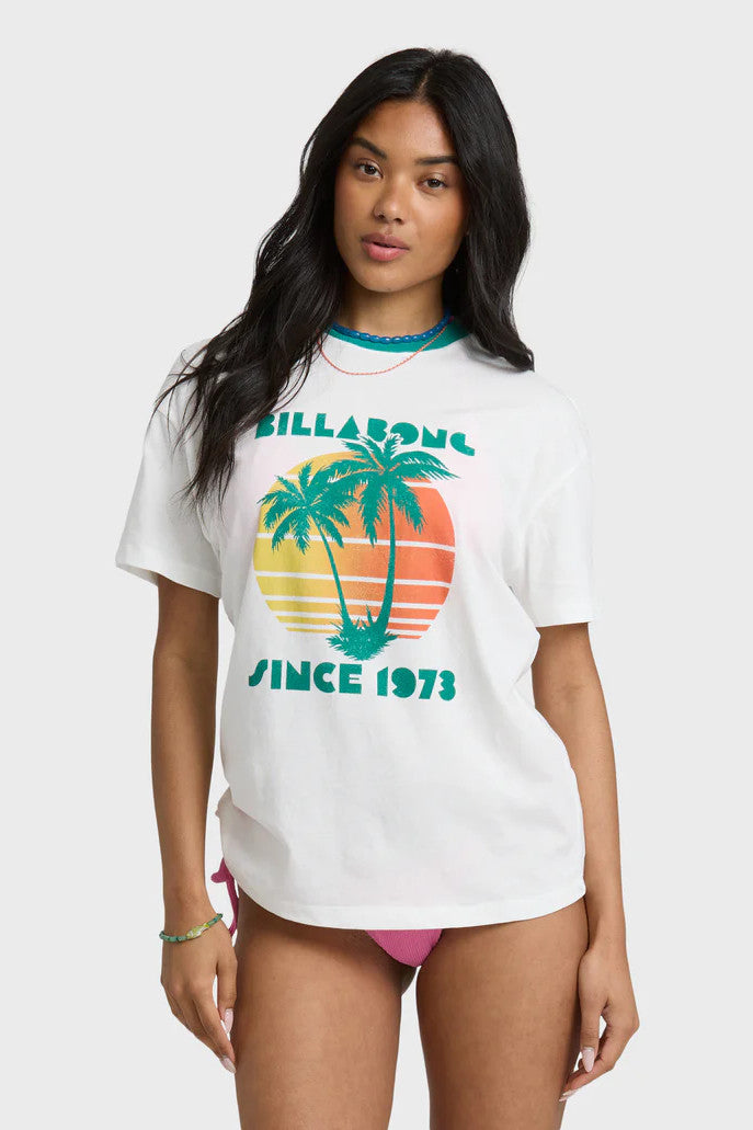 Woman wearing a Billabong t-shirt with a palm tree design and pink bikini bottoms on a white background