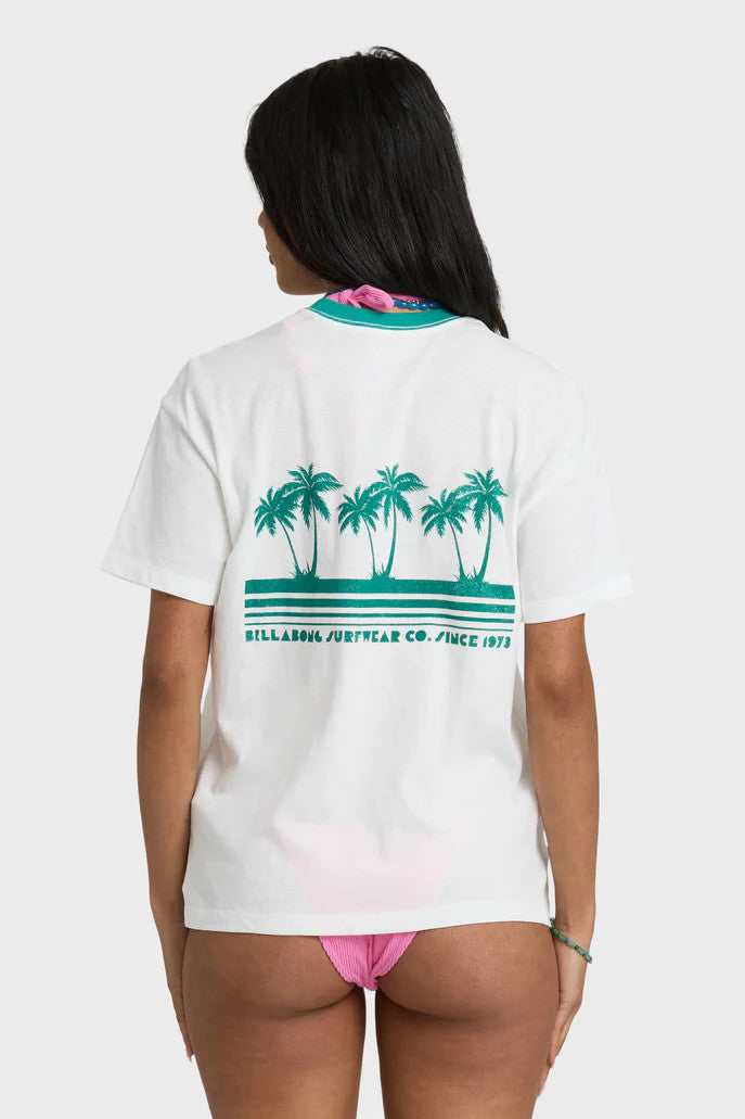 Back of a woman wearing a Billabong t-shirt with a palm tree design and pink bikini bottoms on a white background