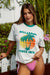 Woman wearing a Billabong t-shirt with a palm tree design and pink bikini bottoms outdoors.