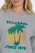 Woman wearing a gray sweatshirt with a palm tree design and 'Billabong Since 1973' text on a white background