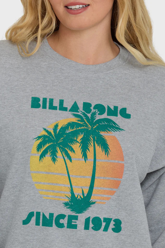 Woman wearing a gray sweatshirt with a palm tree design and 'Billabong Since 1973' text on a white background
