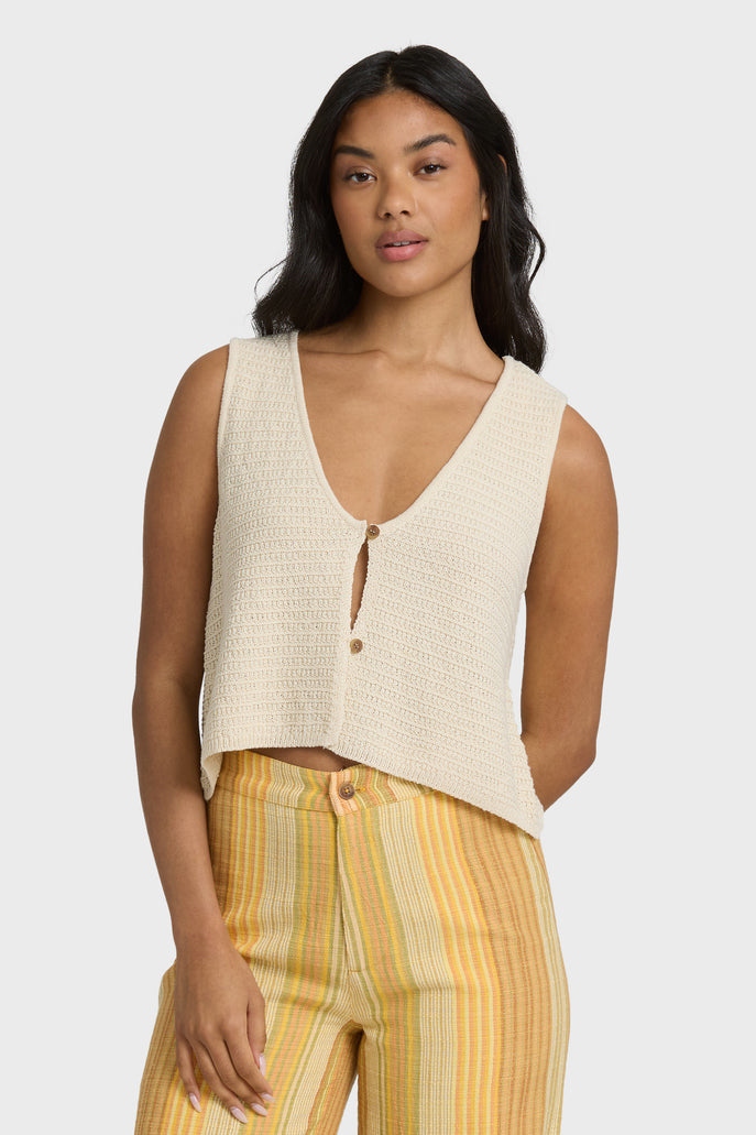 Woman wearing a beige knit tank with yellow striped pants on a white background