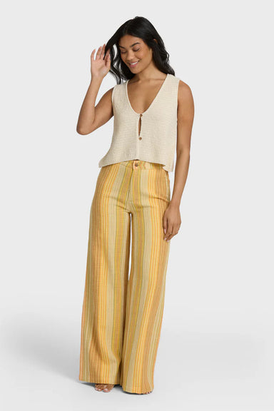 Woman wearing a beige sleeveless top and yellow striped pants on a white background