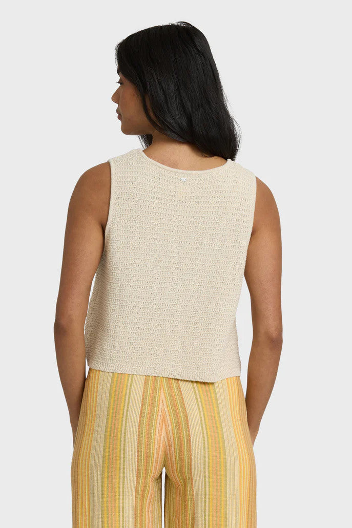 Back view of a woman wearing a beige knit tank with yellow striped pants on a white background