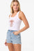 Woman wearing a white tank top with a palm tree design and denim shorts on a white background