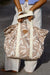 Person holding a patterned tote bag with white straps on a blurred background