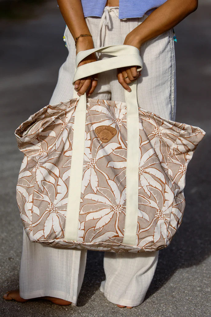 Person holding a patterned tote bag with white straps on a blurred background