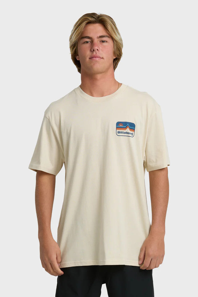 A man wearing a beige t-shirt with short sleeves, featuring a blue and orange mountain and sun graphic on the chest.
