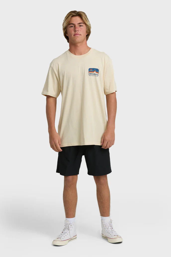 A man wearing a beige t-shirt with short sleeves, featuring a blue and orange mountain and sun graphic on the chest.