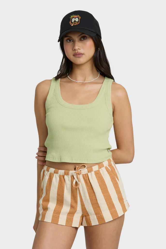 Woman wearing a green tank top and striped shorts with a black cap on a white background