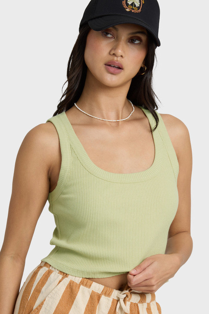 Woman wearing a green tank top and striped shorts with a black cap on a white background