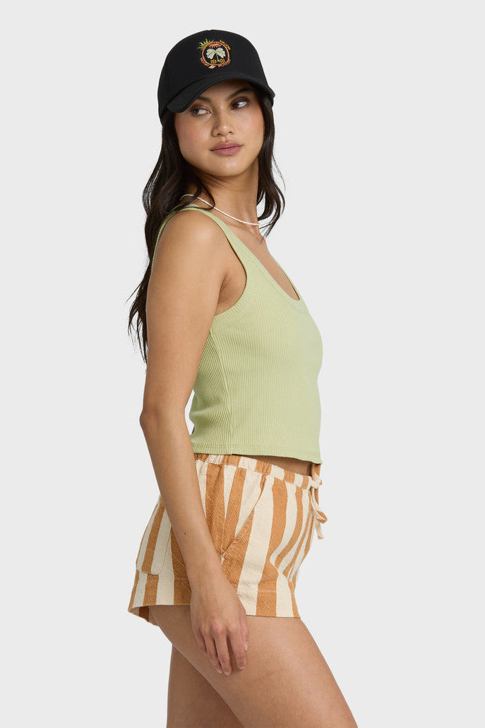 Woman wearing a green tank top and striped shorts with a black cap on a white background