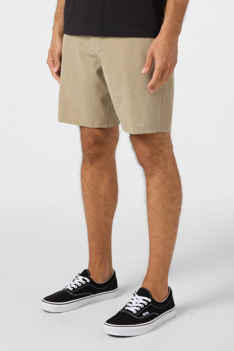 Person wearing beige shorts and black sneakers on a white background