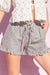 Person wearing a white blouse and striped shorts with a ruffled hem on a pink background