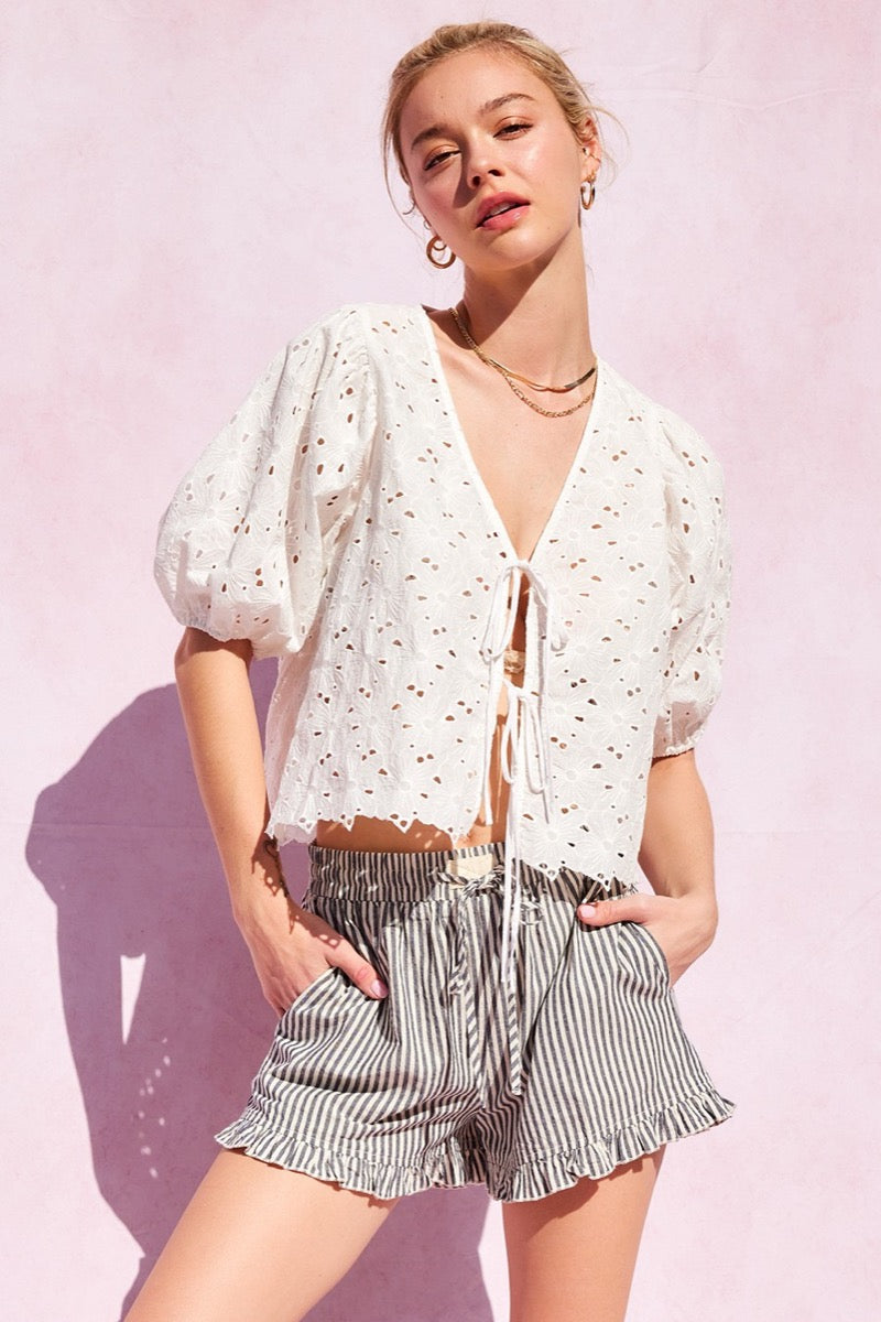 Person wearing a white blouse and striped shorts with ruffled hem on a pink background