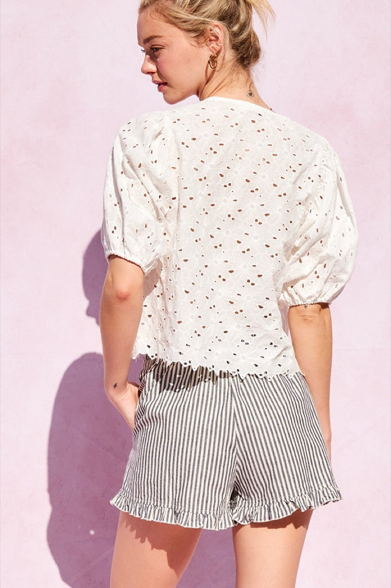 Person wearing a white blouse and striped shorts with ruffled hem on a pink background