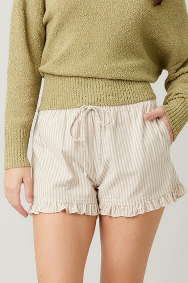 Person wearing a green sweater and beige striped shorts with ruffled hem on a plain background