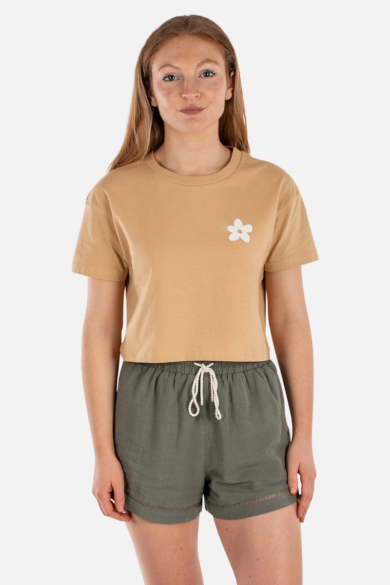 Person wearing a beige t-shirt with a flower design and green shorts on a white background