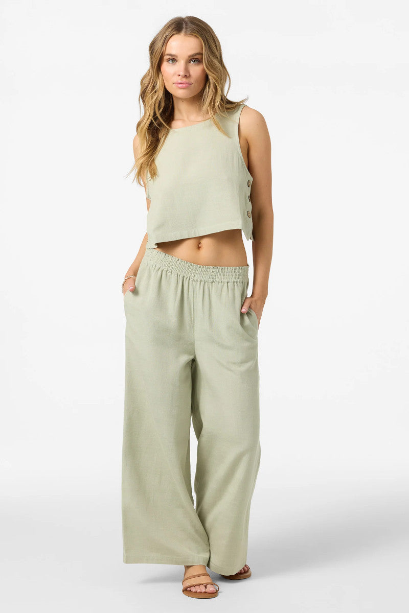 Woman wearing a light green sleeveless top and wide-leg pants on a white background
