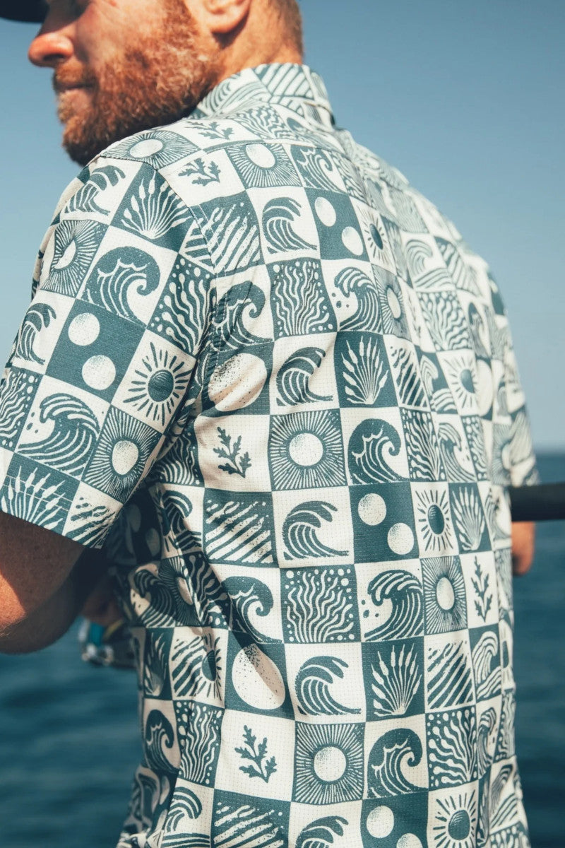 Man wearing a patterned shirt with ocean design, standing by the sea.