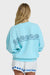 Light blue sweatshirt with decorative patterns on the back worn by a person on a white background